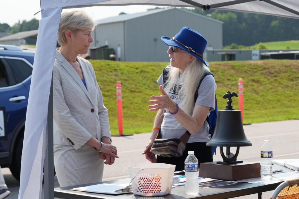 Congresswoman Deborah Ross speaks with Marianne Karth wearing a blue hat at an outdoor event