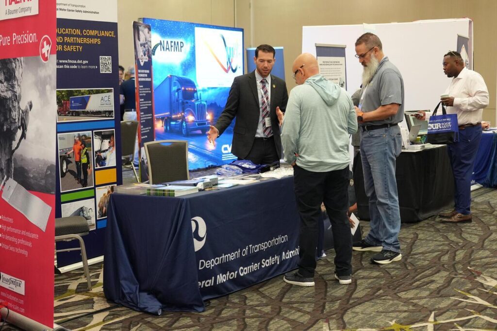 An FMCSA representative speaks with attendees at a Department of Transportation booth during a safety conference