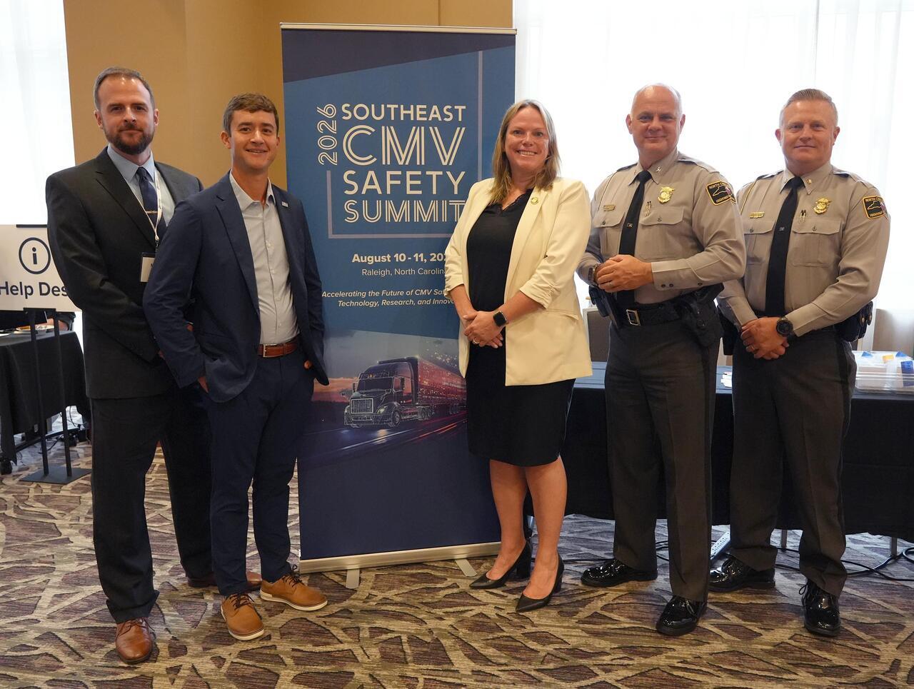 Five people, including two highway patrol officers, pose next to a 2026 Southeast CMV Safety Summit banner