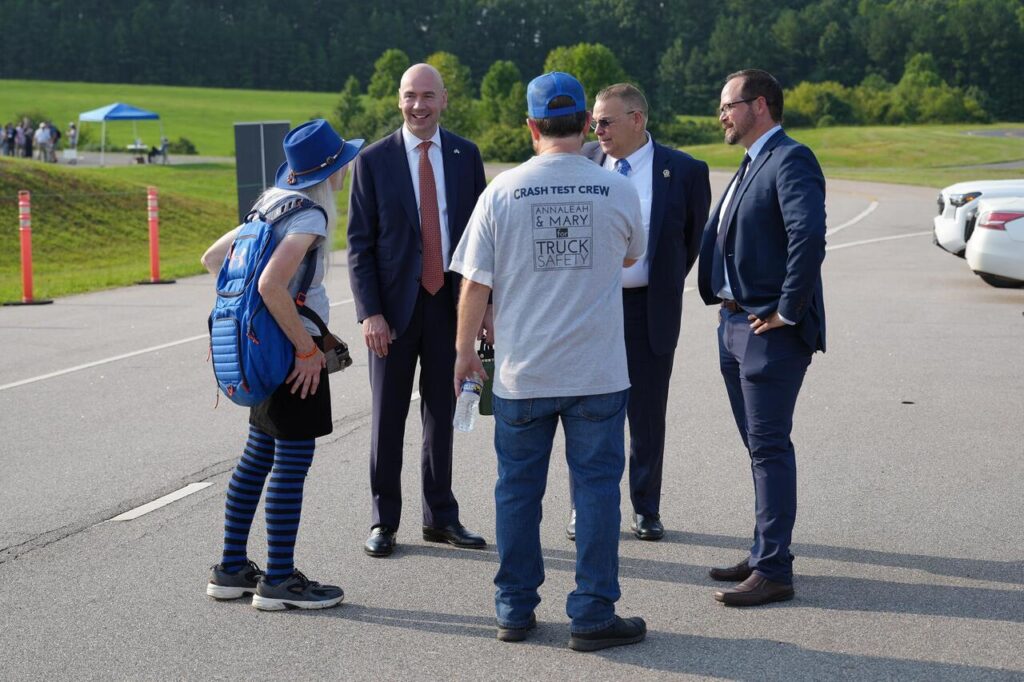 NHTSA Administrator Jonathan Morrison and NHTSA Deputy Administrator Lee White in suits talk with Marianne Karth (AnnaLeah & Mary for Truck Safety Foundation), safety advocates, including one wearing a Crash Test Crew for Truck Safety t-shirt