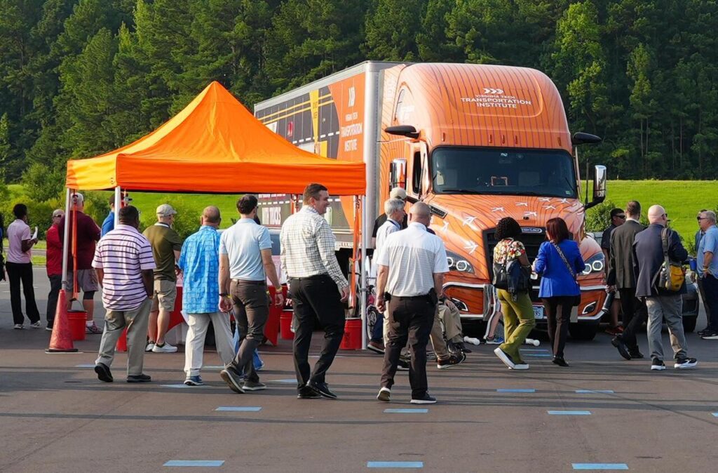 People gather around an orange Virginia Tech Transportation Institute semi-truck and tent at an outdoor event