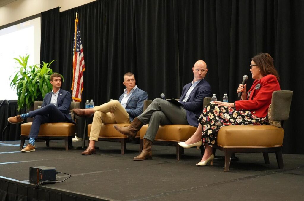 A woman speaks into a microphone during a panel discussion with three men on a stage
