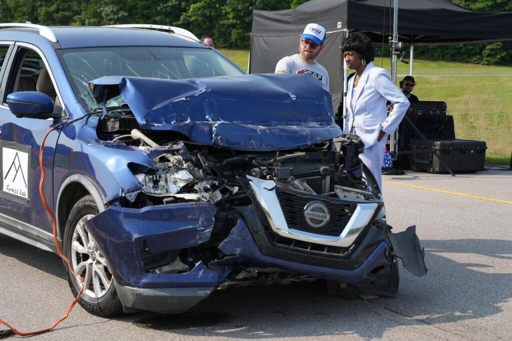A man and Congresswoman Valerie Foushee inspect the severe front-end damage of a blue Nissan SUV